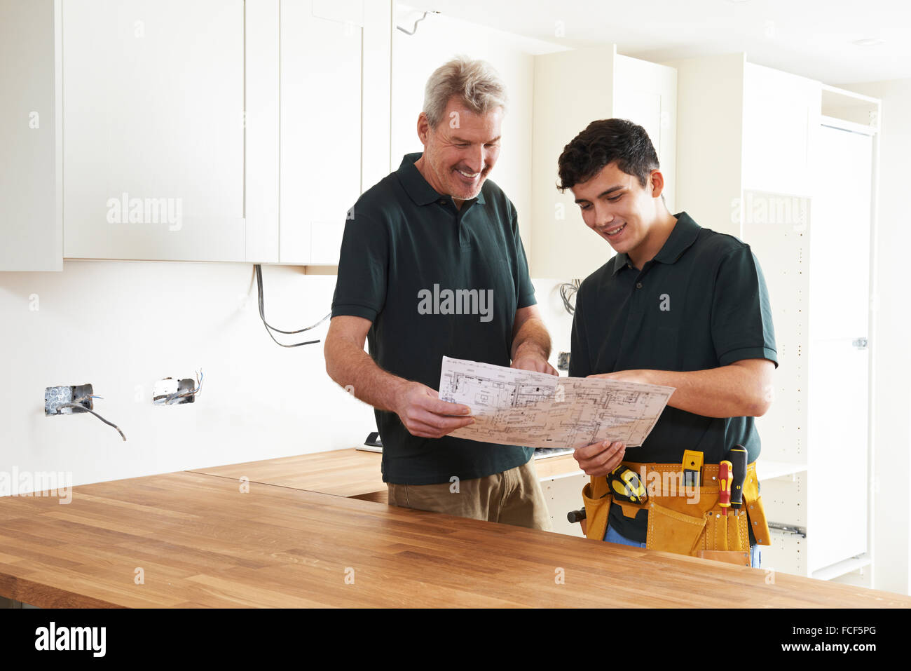 Carpenter And Apprentice Installing Luxury Fitted Kitchen Stock Photo