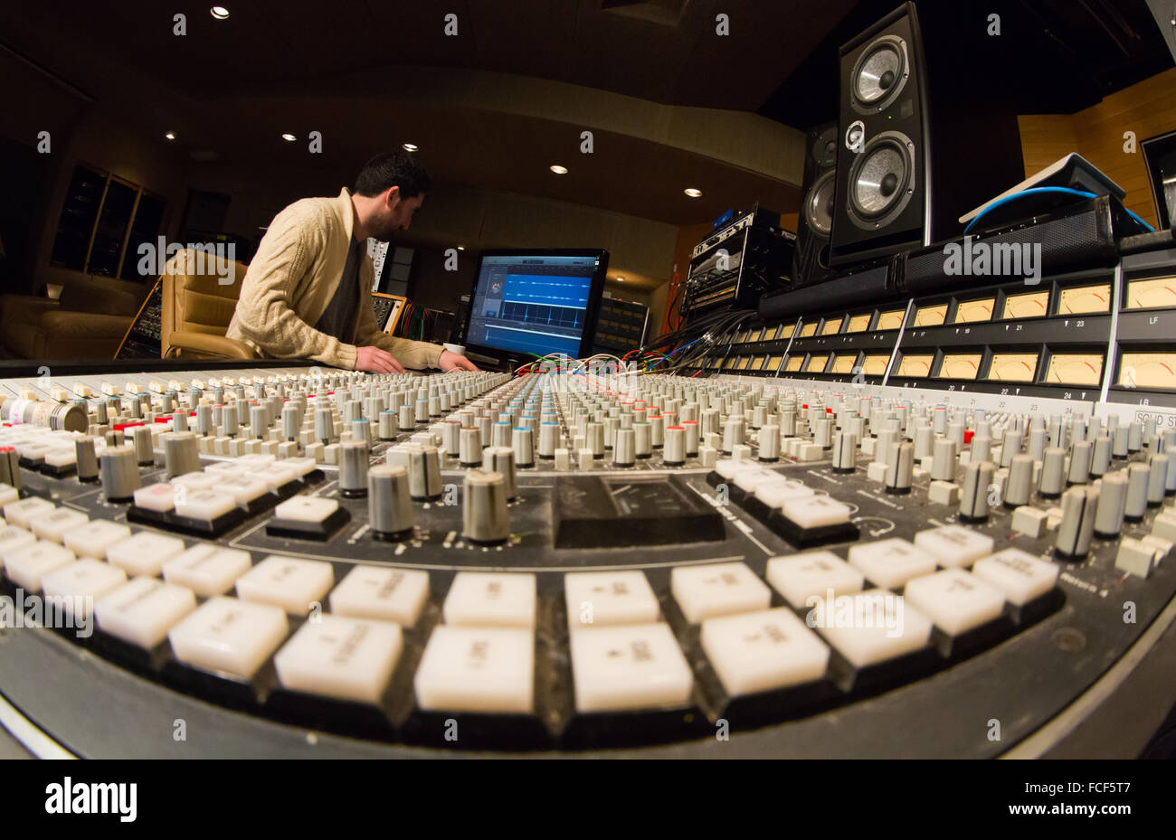 side view of someone working on an ssl e series sound mixing desk and apple mac with studio speakers in a recording studio Stock Photo