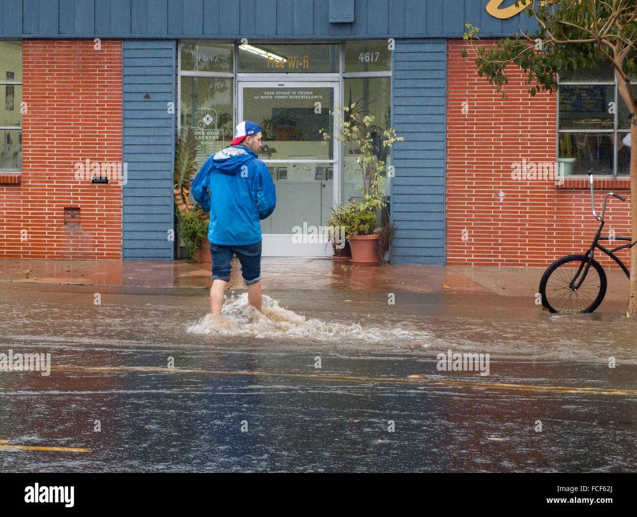 Man without shoes standing on a flooded sidewalk in Pacific Beach next to a laundry, in January 2016. Stock Photo