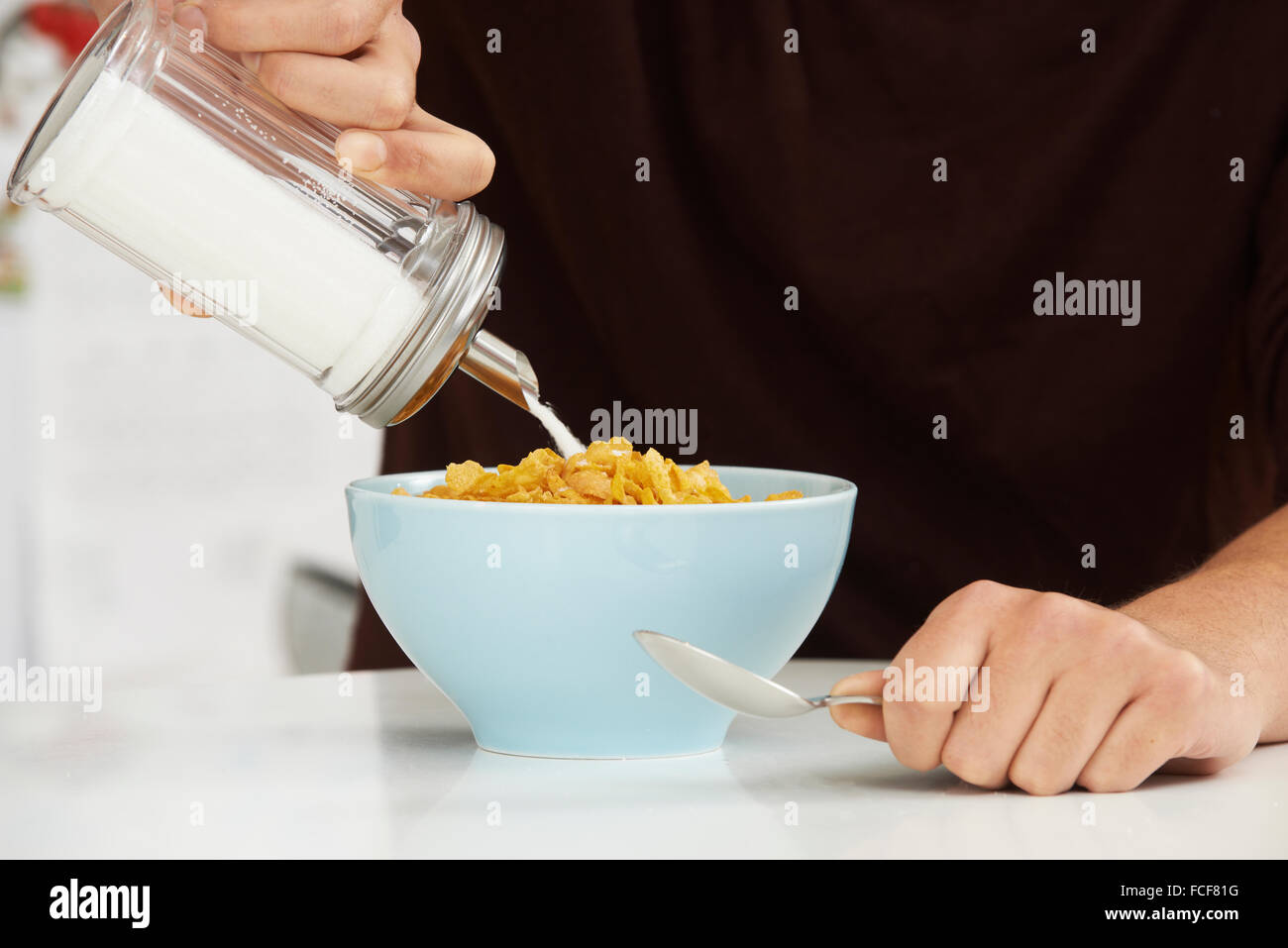 Young Man Adding Sugar To Breakfast Cereal Stock Photo