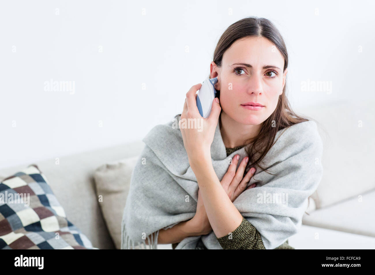 Woman taking her temperature with a digital tympanic thermometer. Stock Photo