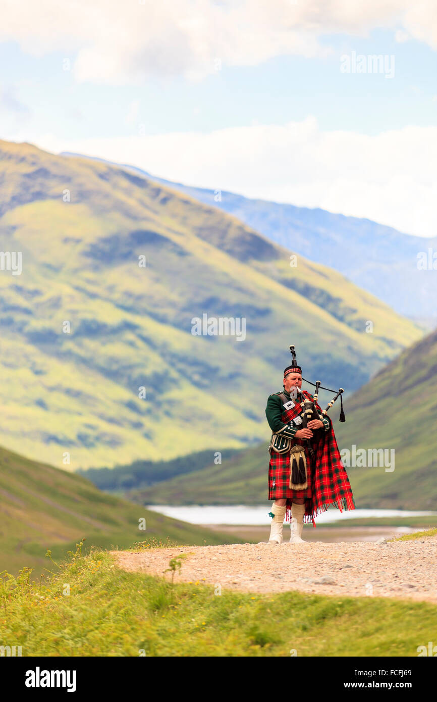Bagpipe player in front of Loch Achtriochtan and steep hills in the background in Glencoe, Highlands, Scotland, UK  Model Release: No.  Property Release: No. Stock Photo