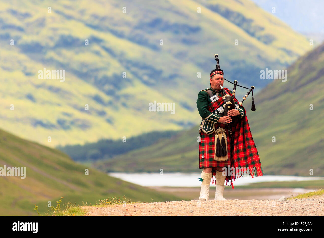 Bagpipe player in front of Loch Achtriochtan and steep hills in the ...