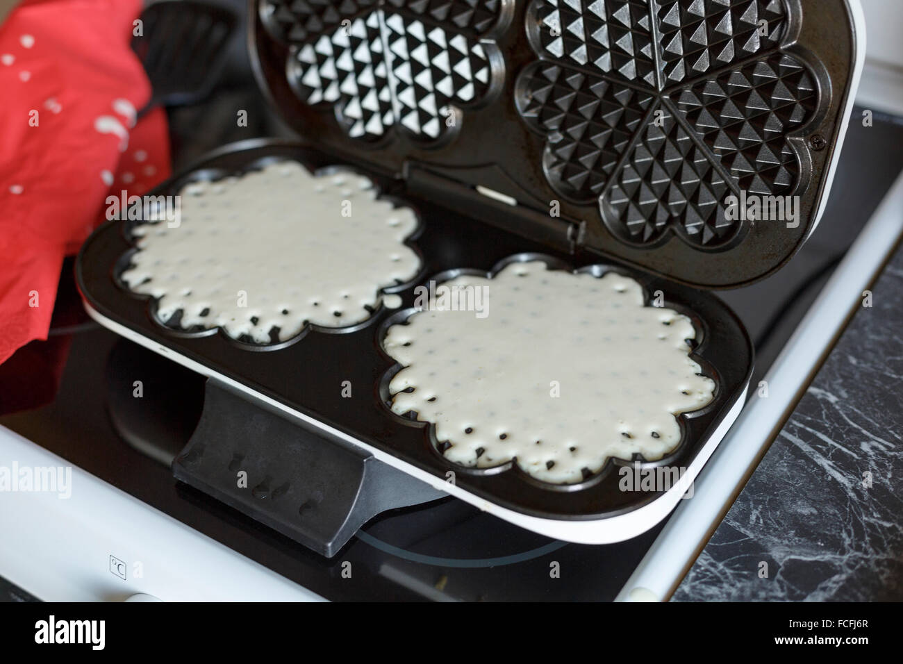 Two homemade waffles on electric waffle maker iron on top of stove in kitchen Stock Photo