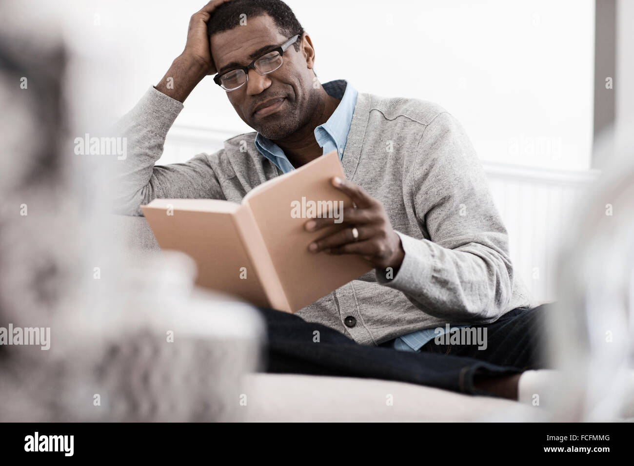 A man sitting on a sofa at home, reading a book Stock Photo Alamy