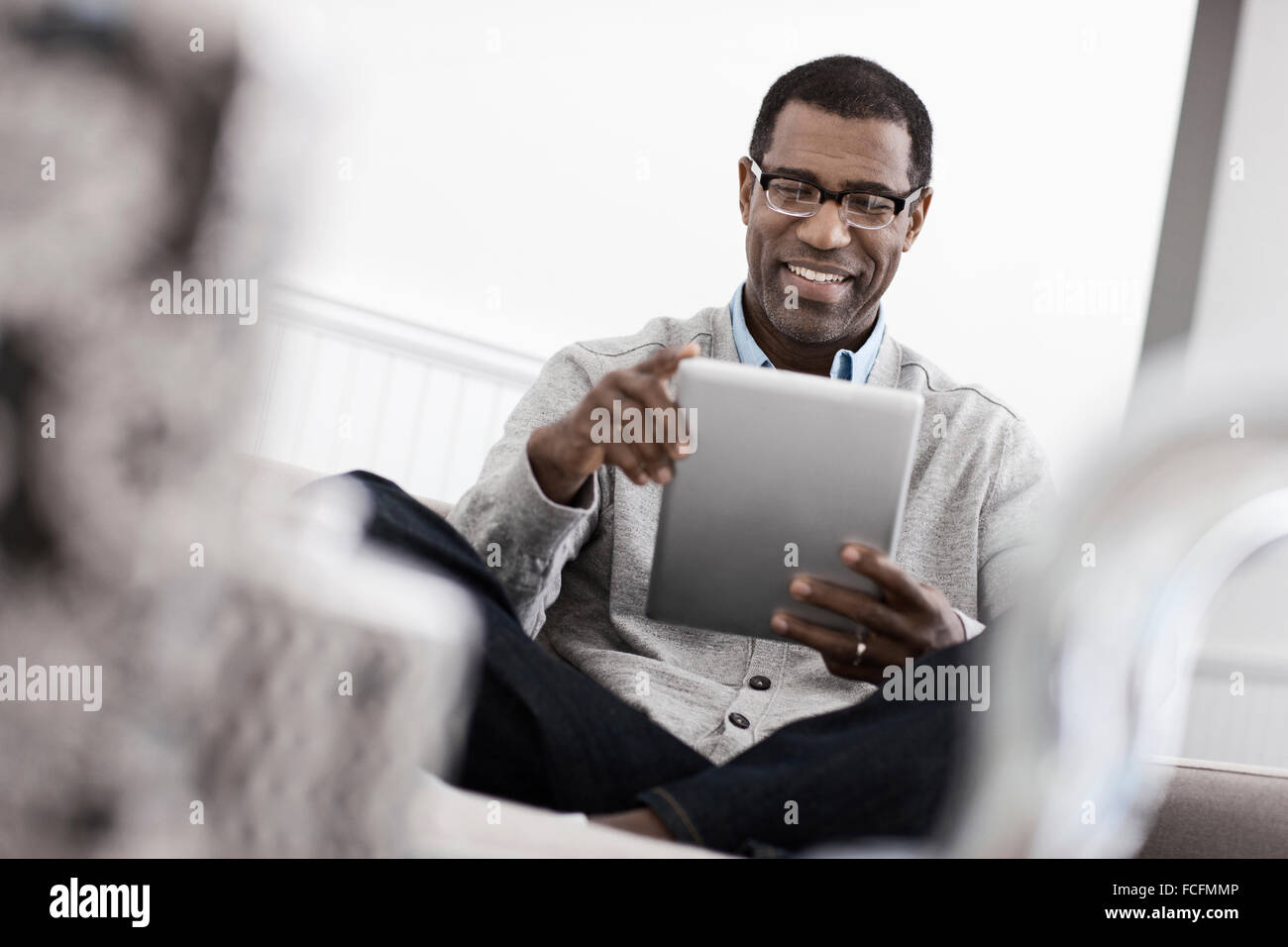 A man sitting on a sofa, using a digital tablet. Stock Photo