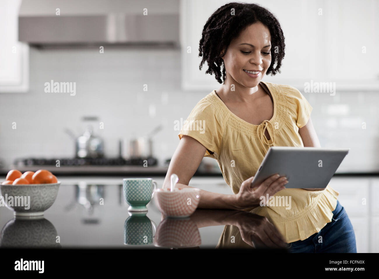 A woman using a digital tablet in her home. Standing in the kitchen. Stock Photo