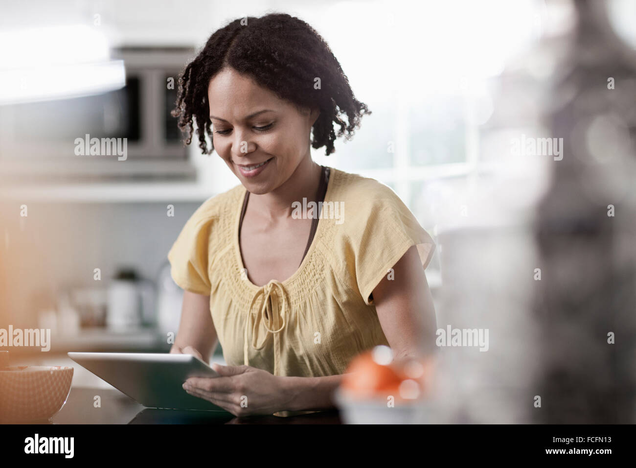 A woman using a digital tablet in her home. Standing in the kitchen. Stock Photo