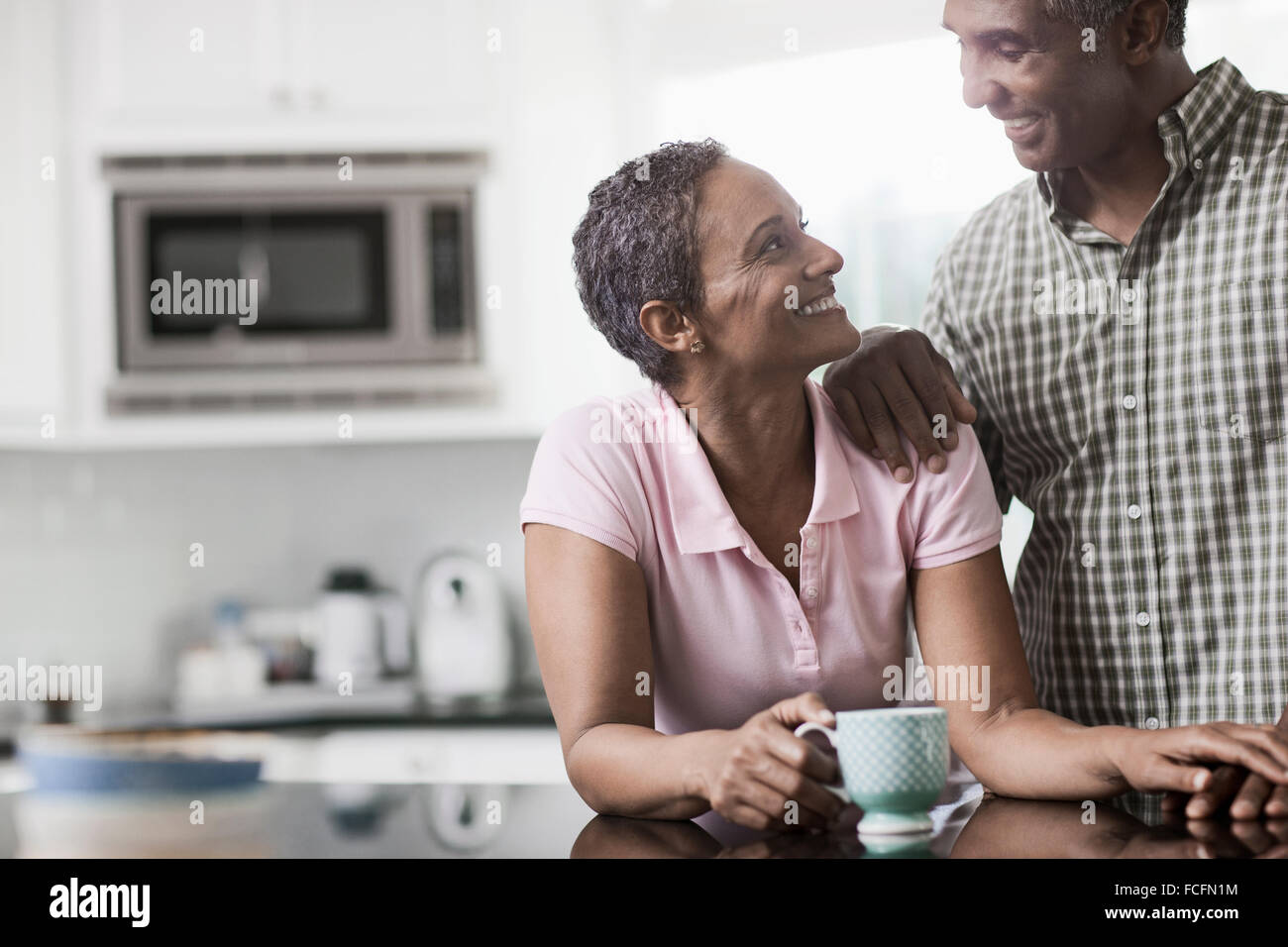 A couple in the kitchen of their home, smiling at each other. Stock Photo