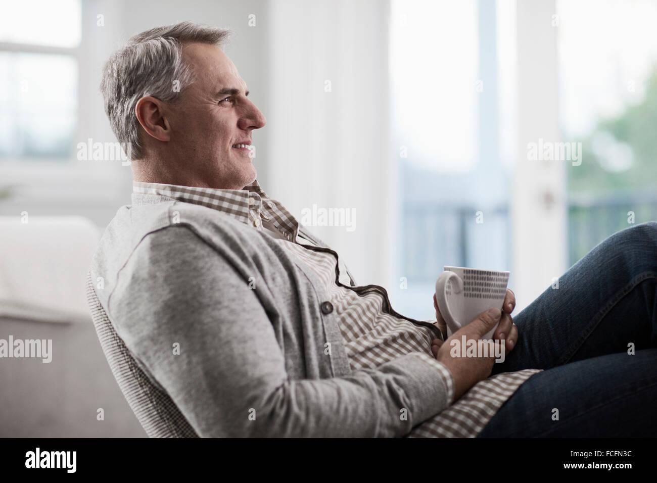 A mature man with grey hair leaning back in a chair, relaxing with a cup of tea or coffee. Stock Photo