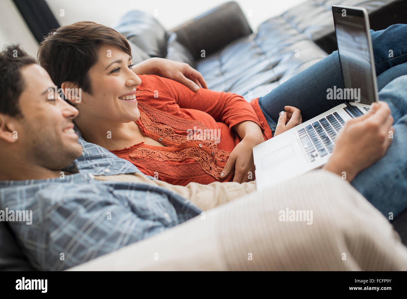 A man and woman sitting on a sofa, looking at the screen of a laptop. Stock Photo