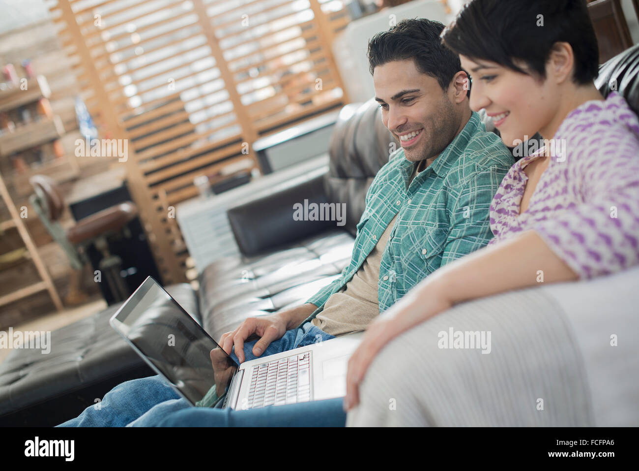 A man and woman sitting on a sofa, looking at the screen of a laptop. Stock Photo