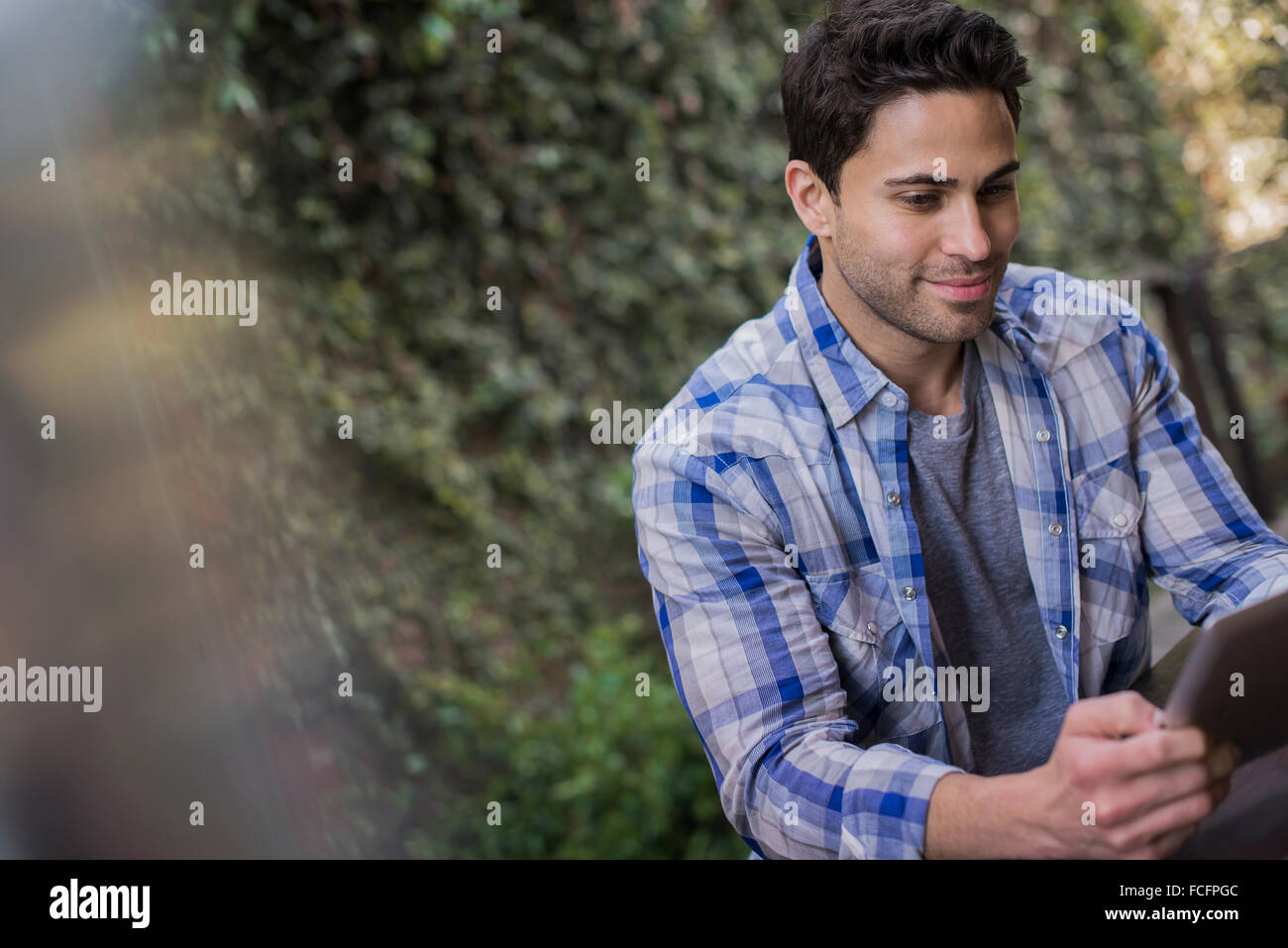 A man sitting at a cafe table outdoors, using a digital tablet. Stock Photo