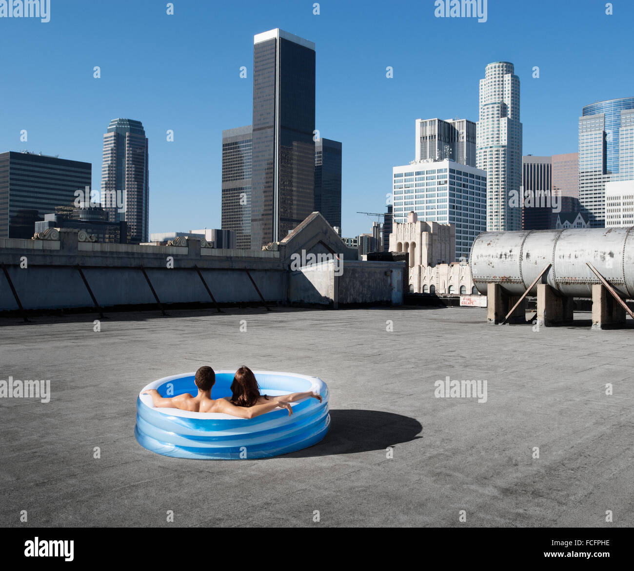A couple, a man and woman sitting in a small inflatable water pool on a city rooftop, cooling down. Stock Photo