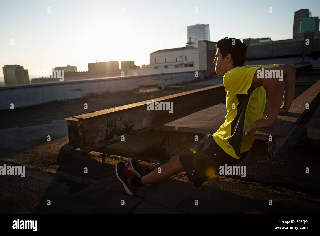 A man in exercise clothes on a rooftop overlooking the city, doing ...