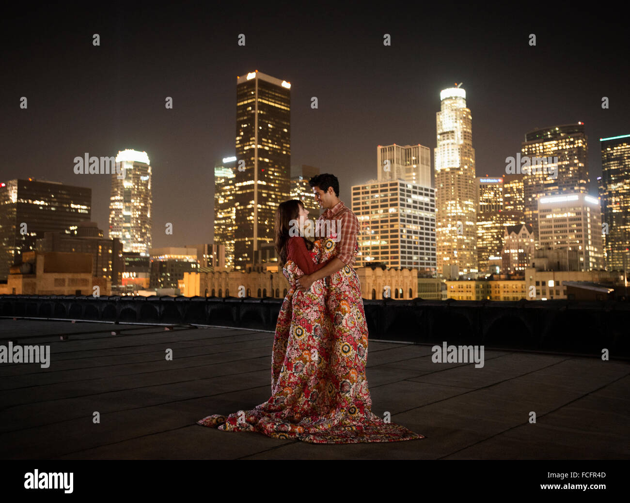A couple on a rooftop overlooking Los Angeles at night, warpped in blankets. Stock Photo