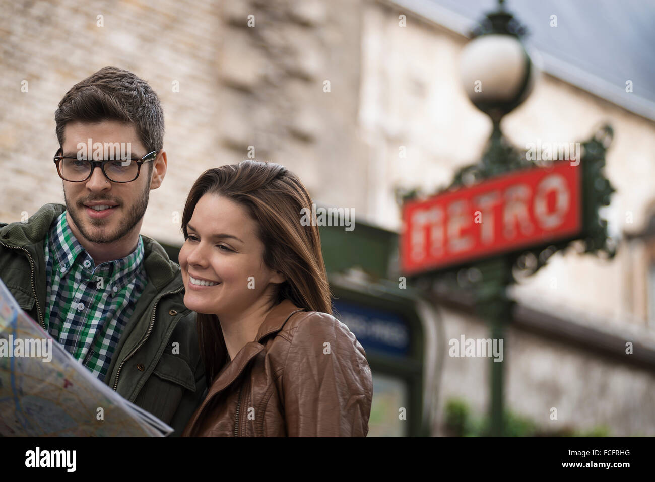 A couple consulting a map on a city street, under a classic Art Deco Metro sign. Stock Photo