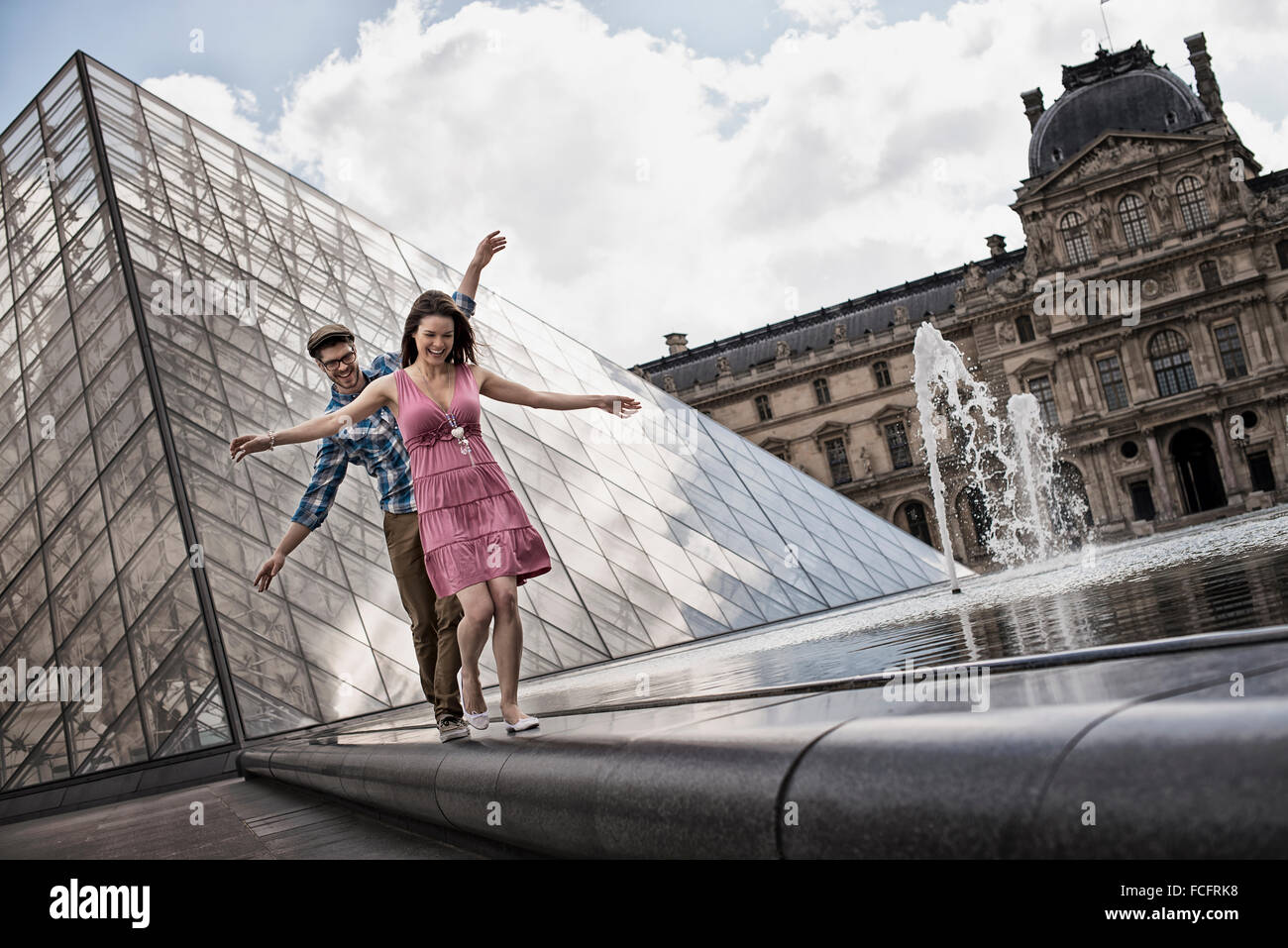 A couple in the courtyard of the Louvre museum, by the large glass pyramid. Water jets and shallow pool. Stock Photo
