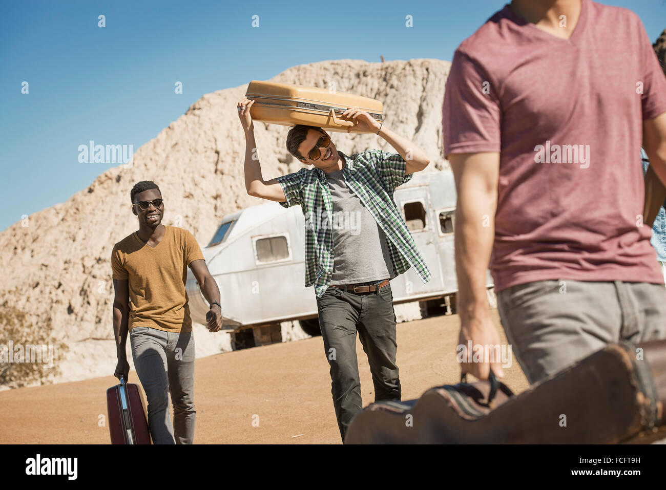 A group of people walking in a line in open desert country, carrying their cases, on a road trip. Stock Photo