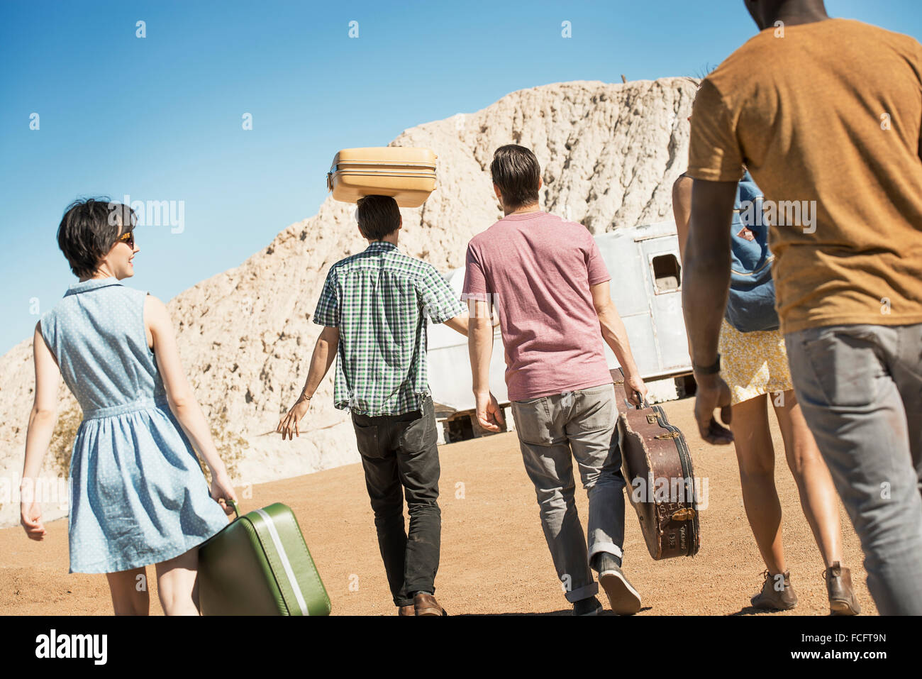 A group of people walking in a line in open desert country, carrying their cases, on a road trip. Stock Photo