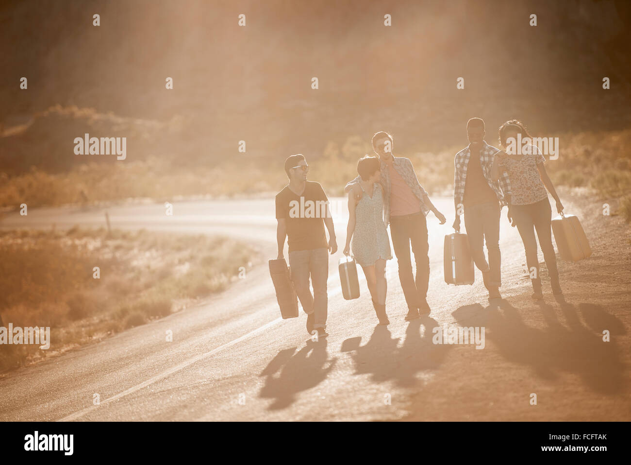 A group of people, men and women, on the road with cases, in open country in the desert. Stock Photo