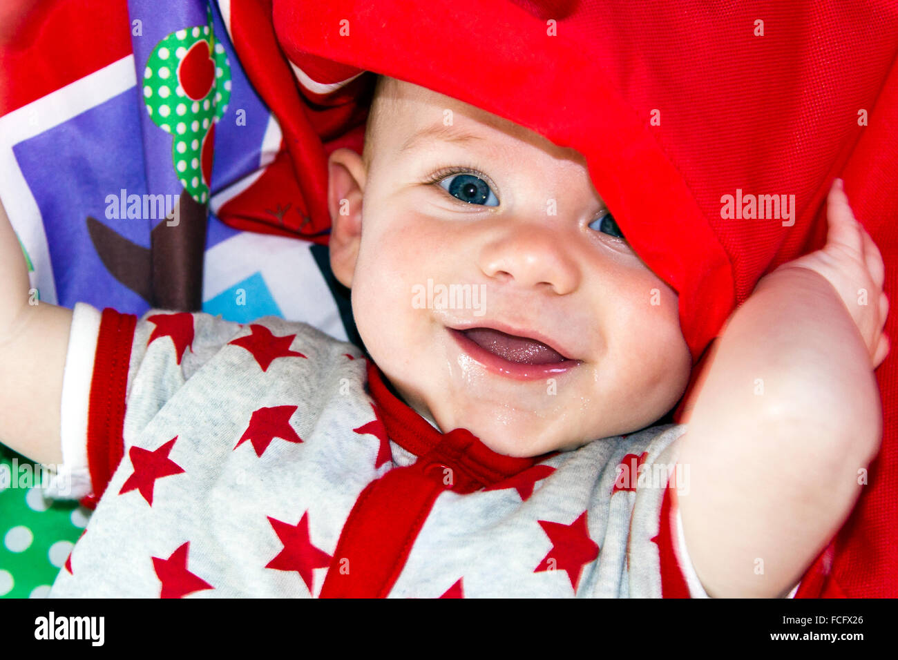 Baby smiling and wrapping himself in his play mat Stock Photo