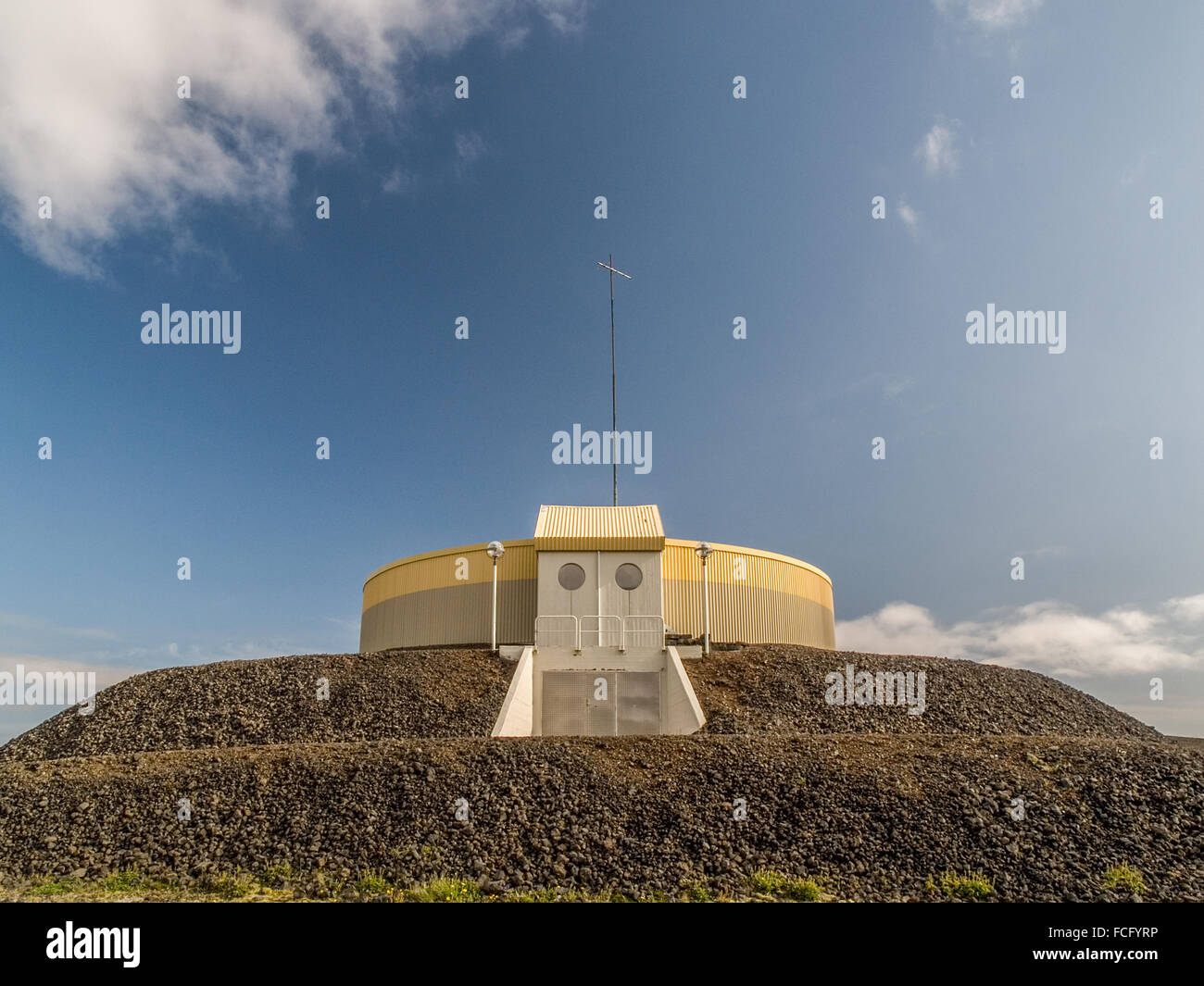 Circular industrial yellow and gray building on top of gravel platform against a blue sky with clouds near Keflavik Iceland. Stock Photo