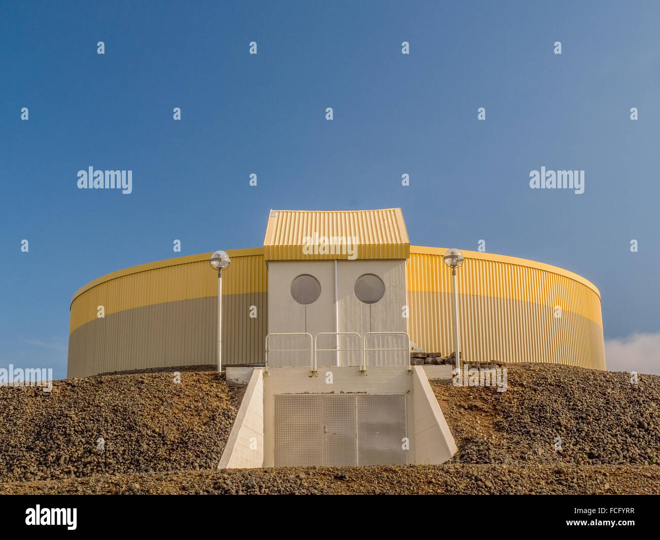 Circular industrial yellow and gray building on top of gravel platform against a blue clear sky near Keflavik Iceland. Stock Photo