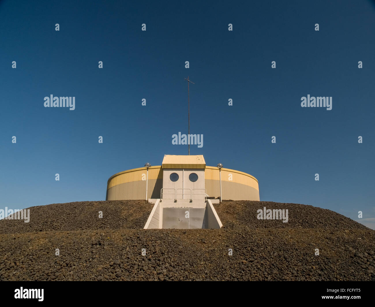 Circular industrial yellow and gray building on top of gravel platform against a blue clear sky near Keflavik Iceland. Stock Photo
