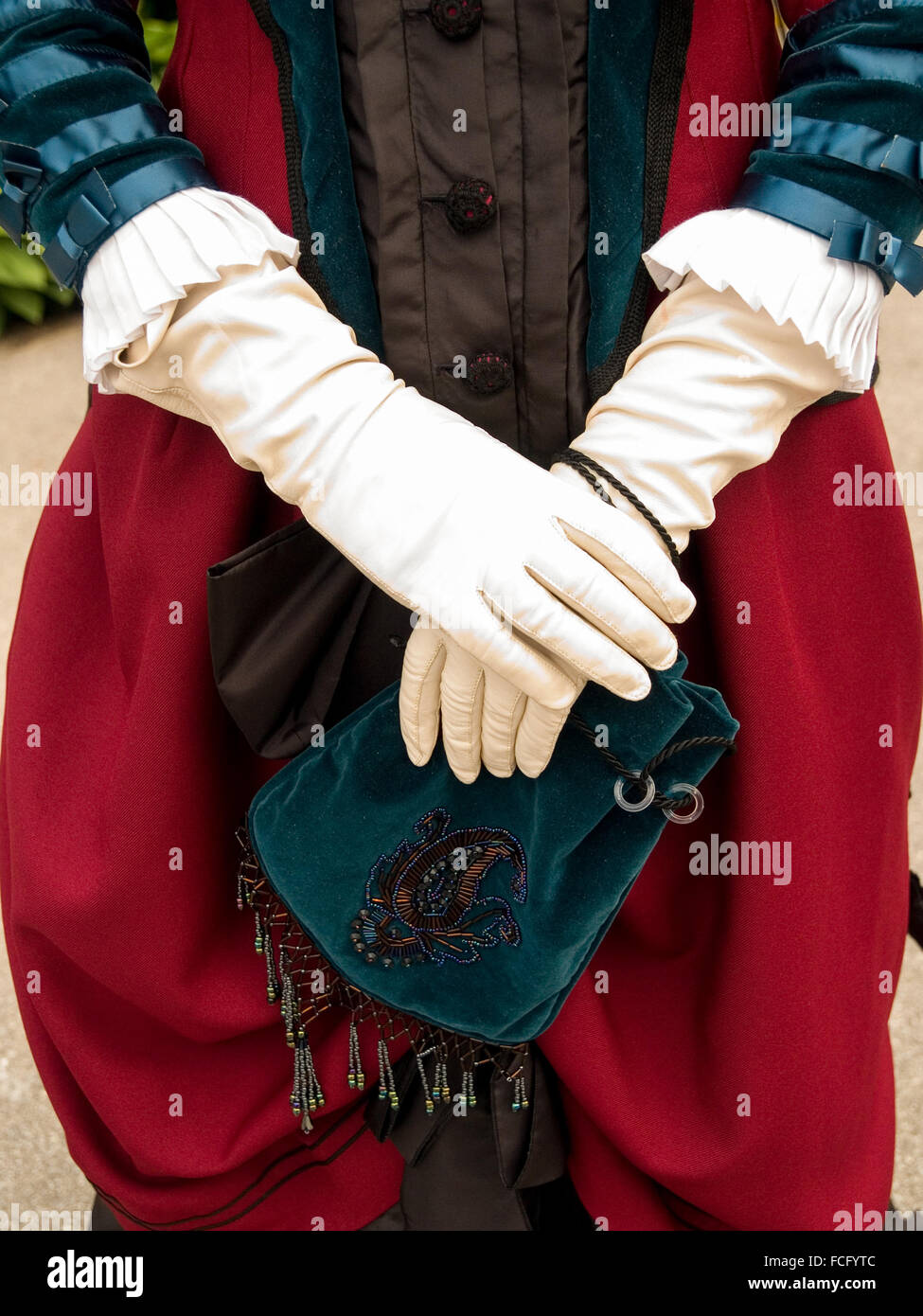 Close up of white gloves and green velvet purse and red victorian velvet dress. Stock Photo