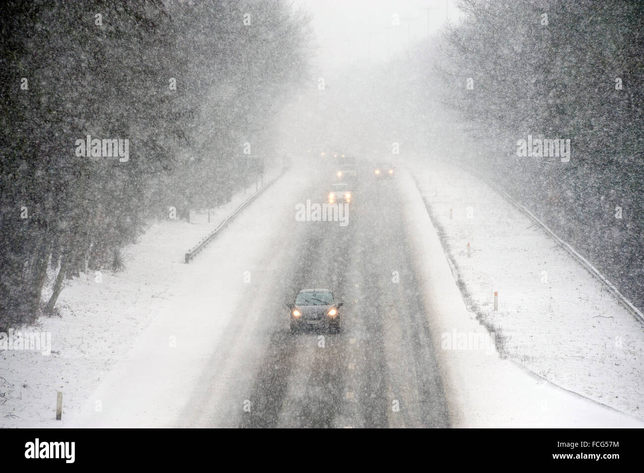 Highway in snowstorm with cars moving slowly on snowy road surface Stock Photo