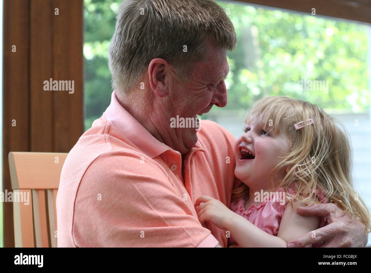 Grandad hugging his little grand-daughter, laughing together sharing a moment of joy and happiness Stock Photo