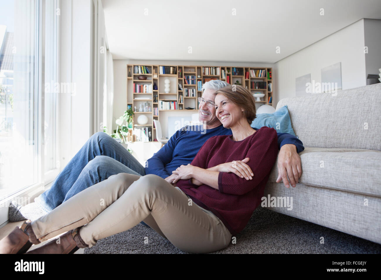Happy couple sitting side by side on the floor of their living room Stock Photo