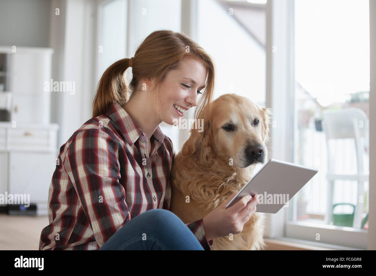 Smiling young woman sitting beside her dog looking at digital tablet Stock Photo