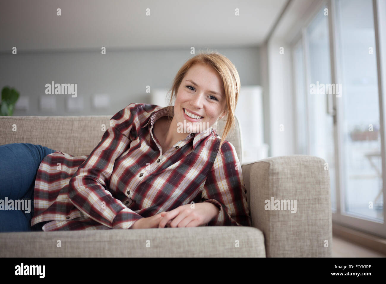 Portrait of smiling young woman lying on couch at home Stock Photo - Alamy