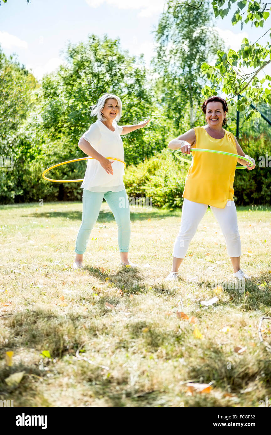 Happy mature women practising   hula hoops on meadow Stock Photo