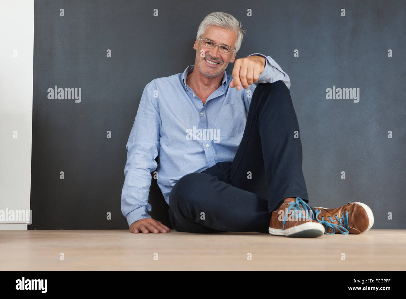 Portrait of smiling mature man sitting on the floor in front of a grey ...