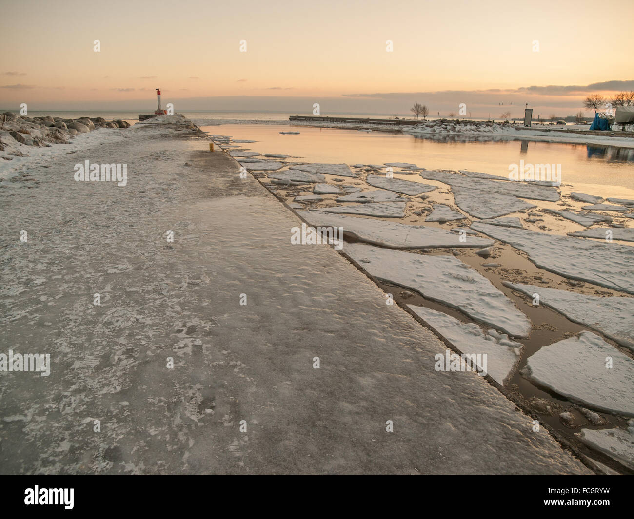 Ice covered pier and Lake Ontario and lighthouse at sunset in winter in Oakville, Ontario, Canada. Stock Photo