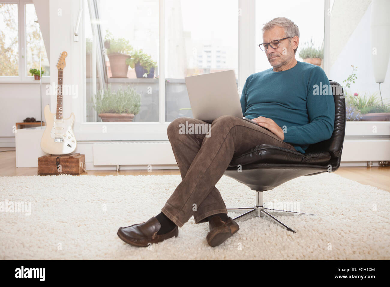 Mature man at home sitting in chair using laptop Stock Photo