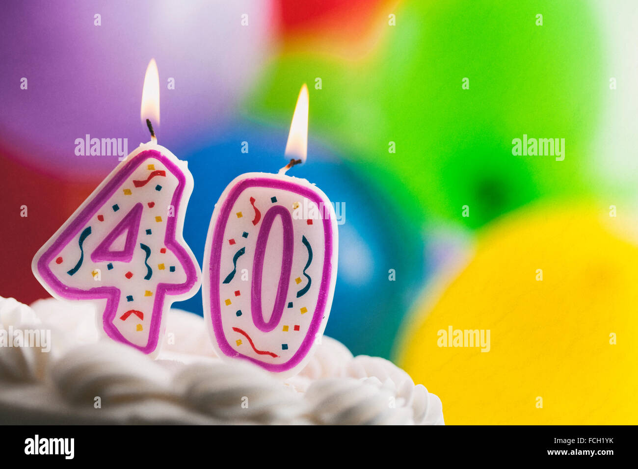 Lighted birthday candles on a cake in front of balloons Stock Photo - Alamy