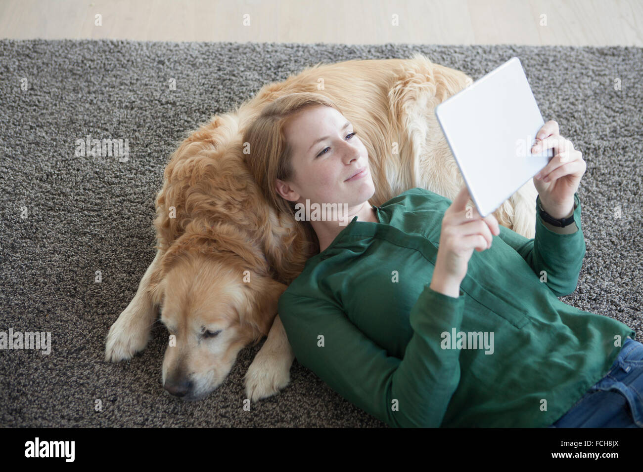 Smiling young woman lying   her dog on the carpet using digital tablet Stock Photo