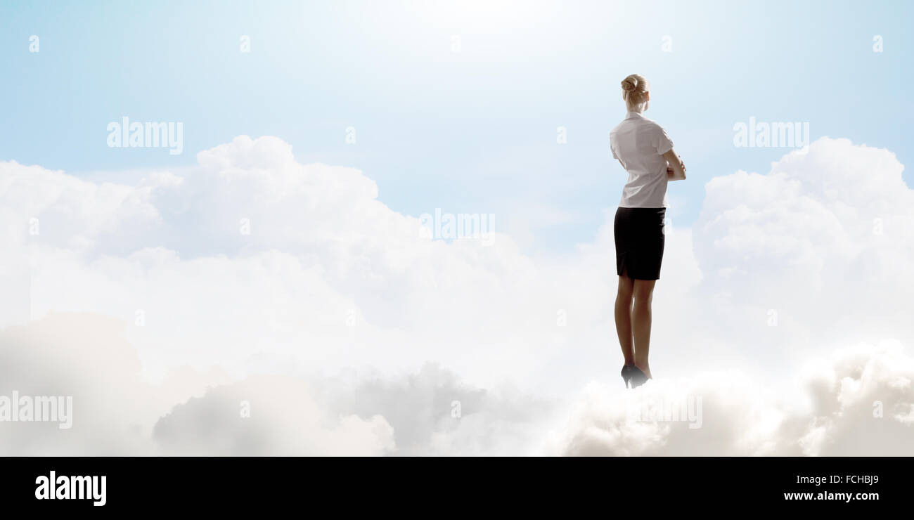 Rear view of businesswoman standing on cloud high in sky Stock Photo ...