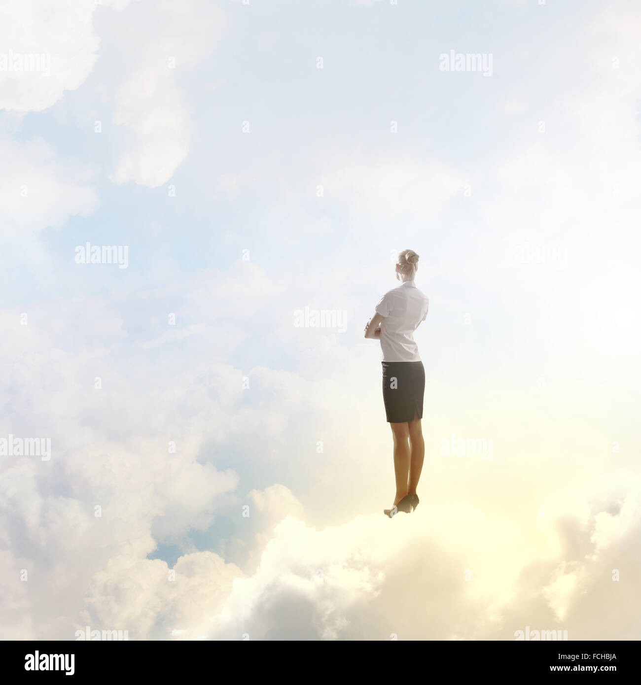 Rear view of businesswoman standing on cloud high in sky Stock Photo ...