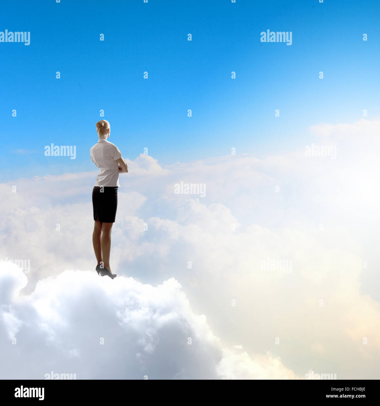 Rear view of businesswoman standing on cloud high in sky Stock Photo ...