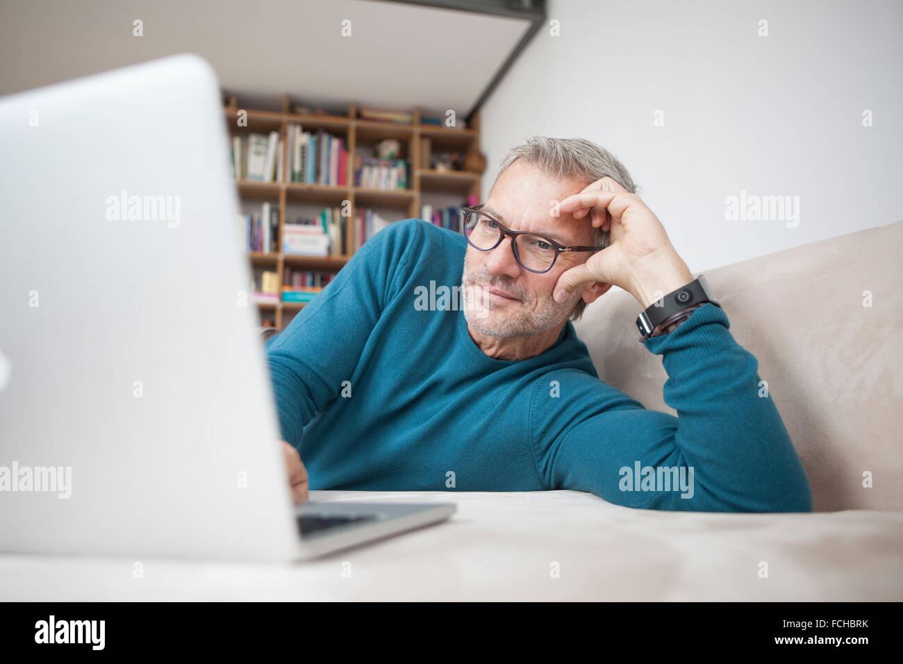 Mature man at home lying on couch using laptop Stock Photo - Alamy