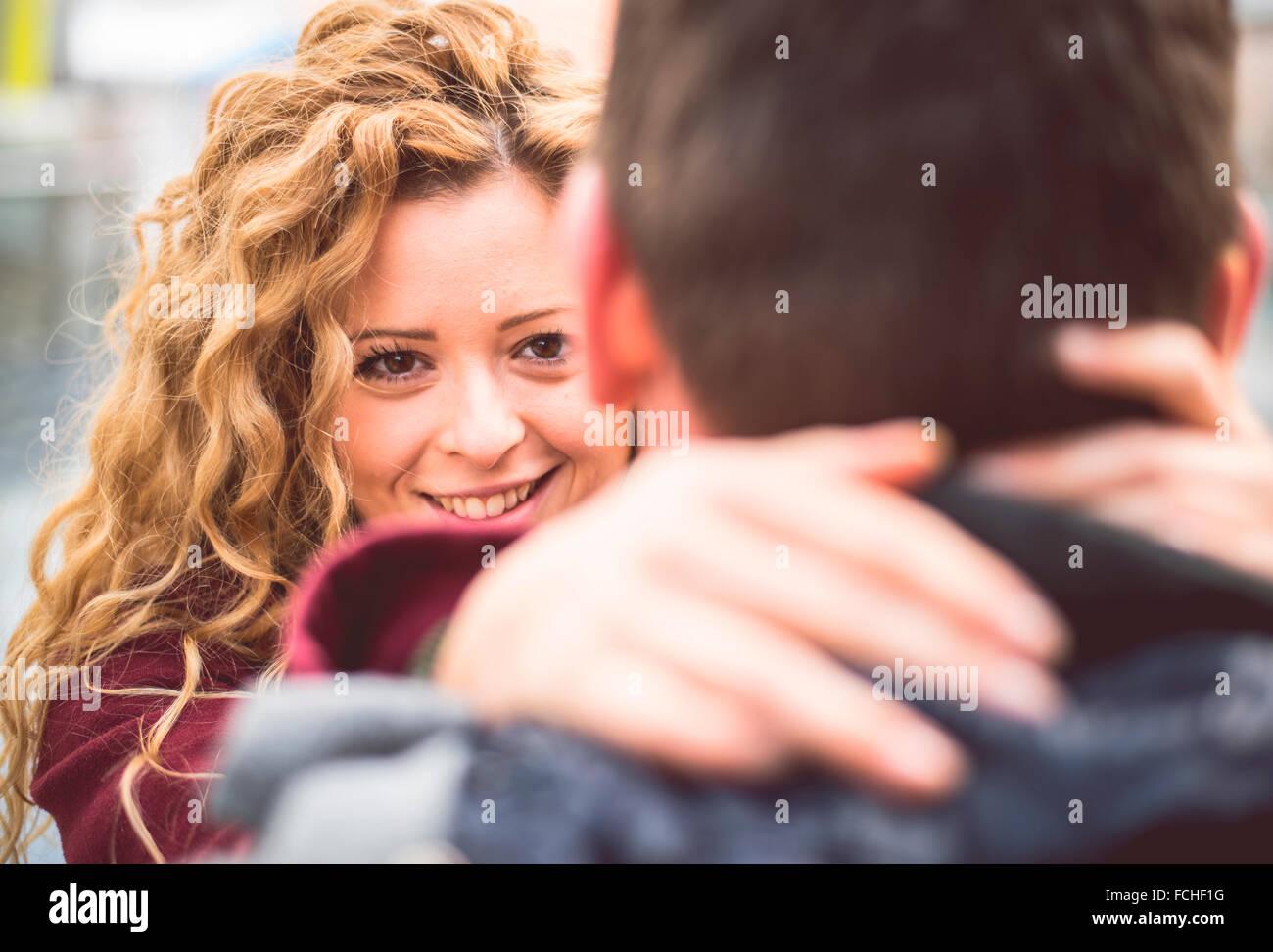 Portrait of smiling young woman hugging her boyfriend while looking at ...