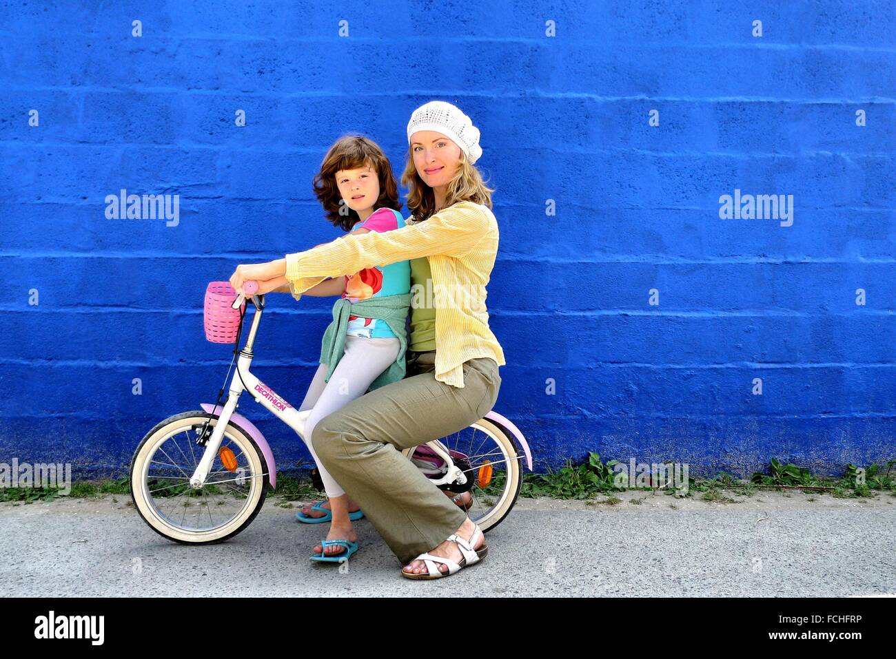7 years old girl on bicycle and her mother front a blue wall in Caños de Meca, Cádiz, Andalucia, Spain Stock Photo