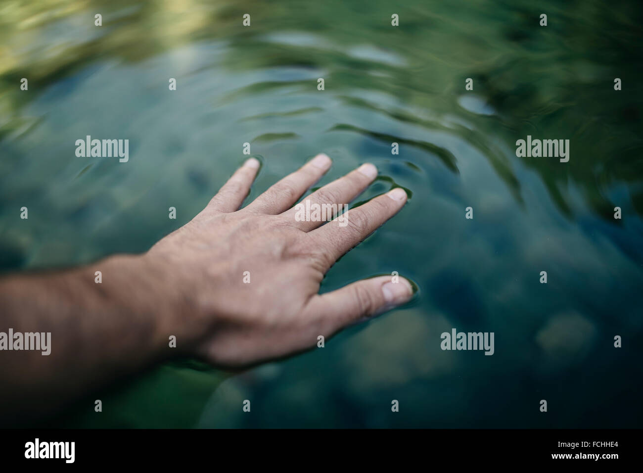 Man's hand touching water surface of a mountain pond Stock Photo