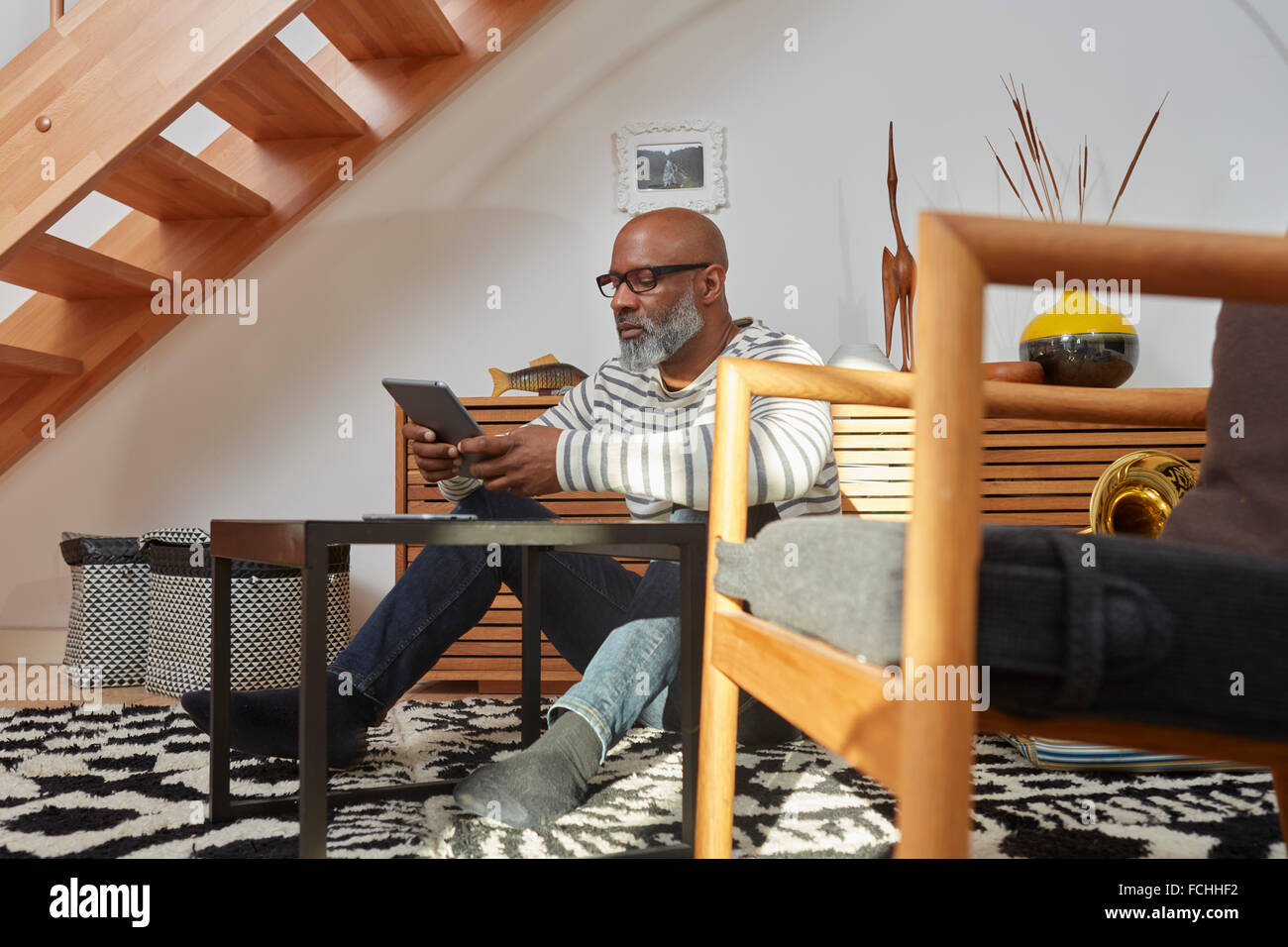 Man sitting on the floor of his living room using digital tablet Stock Photo