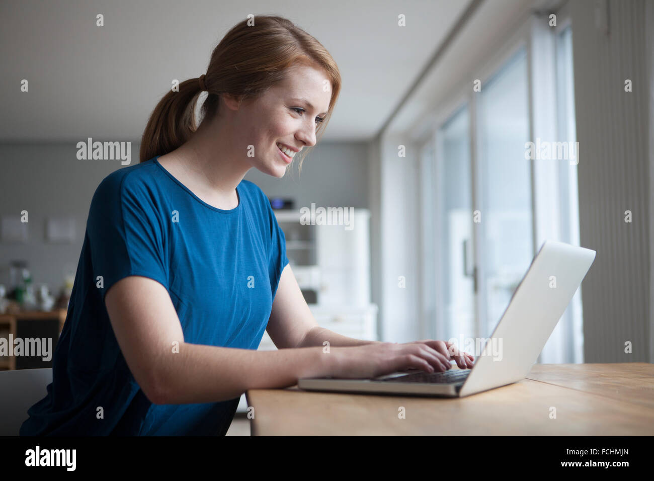 Smiling young woman sitting at table using laptop Stock Photo